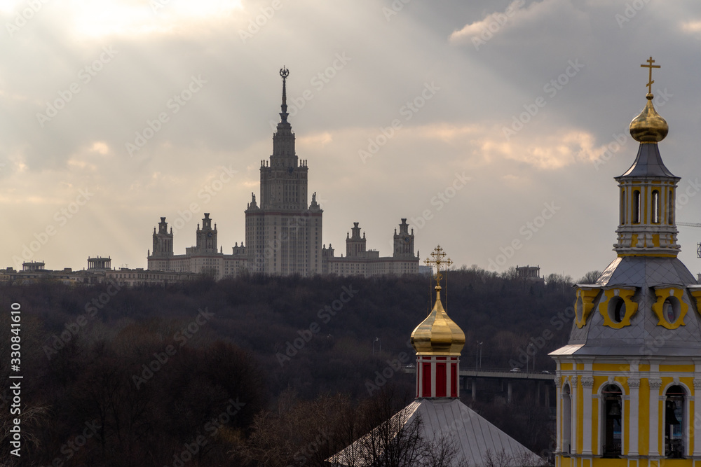 The main building of Moscow State University on the background of the temple, the rays of the sun