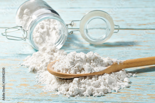 Pour  cornstarch from a glass jar into a wooden spoon, close-up.