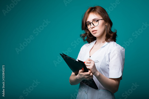 Attractive European doctor looking seriously at camera and recording new symptoms of her patient's illness