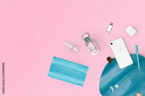 Flat layout of necessary items inside woman purse including protective medical mask. Pink background