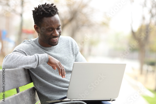 Happy black man using a laptop in a park