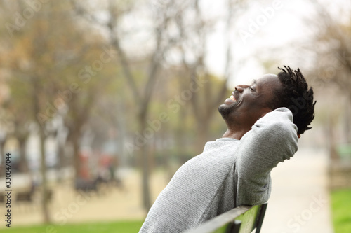 Happy black man relaxing on a bench in a park photo