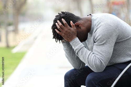 Sad depressed black man on a bench in a park
