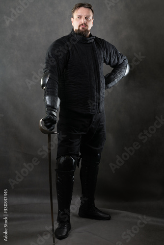 A man with a beard with a sword. Historical European Martial Arts, armor and weapons for practice. gray background studio shooting.