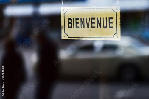 closeup of an old signboard with the text bienvenue, open welcome written in french, on the street in front of a store or a restaurant
