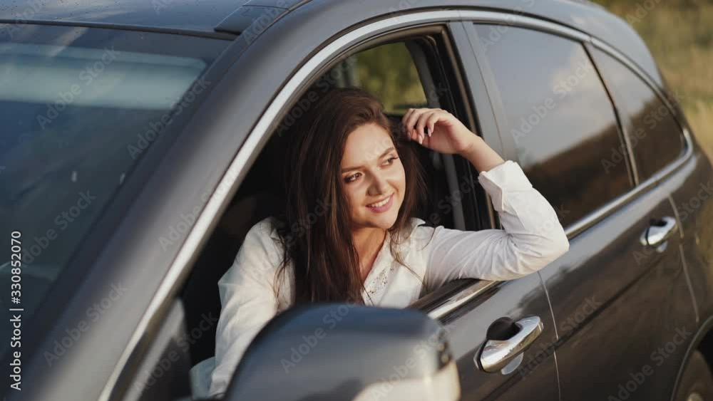 Pretty girl leans out car window, looks outside and smiles Pretty girl leans out car window, looks outside and smiles