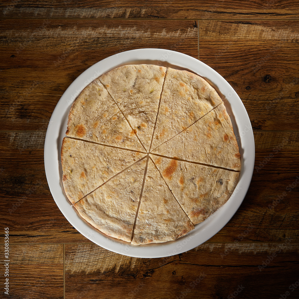 Flatlay of Italian pizza on wooden background. Large pita cut into pieces. Healthy bread. Cutting knife. Basis for pizza. Preparation for pizza Flatlay of Italian pizza on wooden background. Large pita cut into pieces. Healthy bread. Cutting knife. Basis for pizza. Preparation for pizza