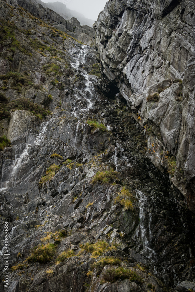 Looking up at rock face with water falling to misty mountain edge