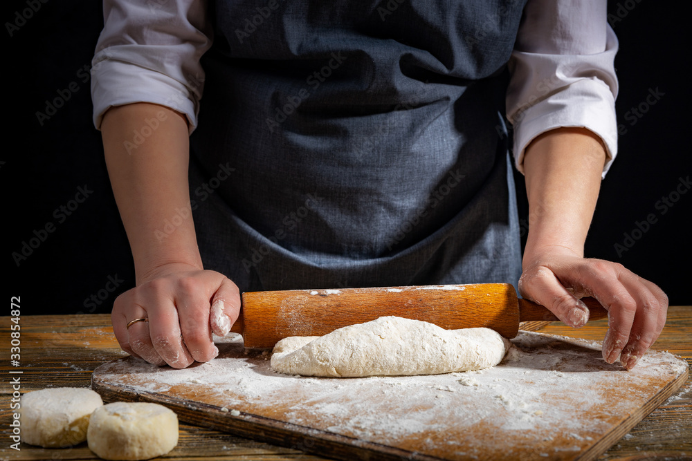 Female hands knead the dough on a wooden antique table on a dark background, close-up, shallow depth of field, beautiful directional lighting. Concept of home baking and comfort. Female hands knead the dough on a wooden antique table on a dark background, close-up, shallow depth of field, beautiful directional lighting. Concept of home baking and comfort.
