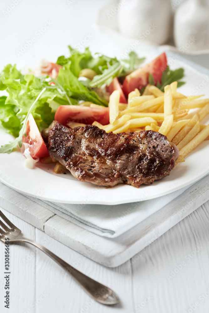 Grilled Steak with french fries and fresh salad. White wooden background. Grilled Steak with french fries and fresh salad. White wooden background.