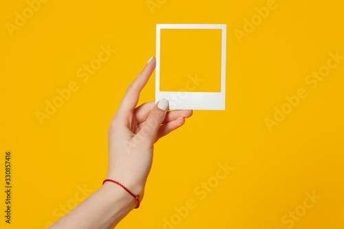 female hand holds empty instant photo frame isolated on yellow background