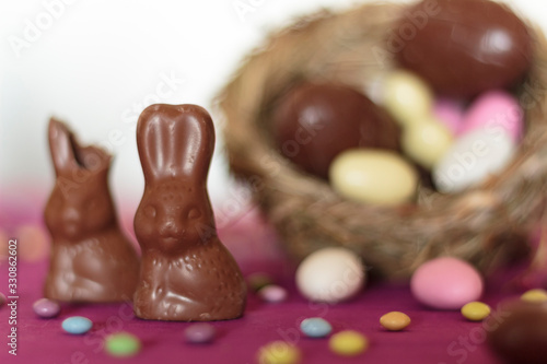 Chocolate bunnies, one missing a bite, and bird nest with easter sweets on the background photo