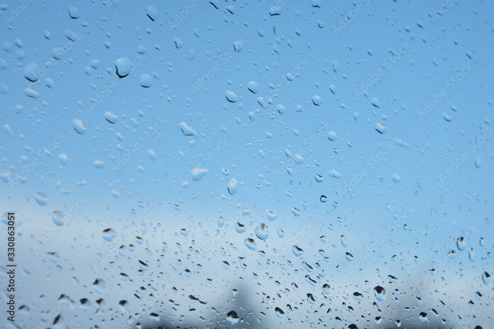 Small raindrops on glass with a blue background behind it. Horizontal orientation. Background, texture Small raindrops on glass with a blue background behind it. Horizontal orientation. Background, texture