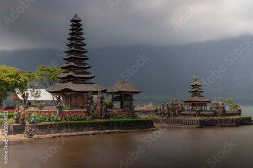 Clouds and mist descend on distant tropical mountains as the famous Hindu temple on the lake offers a destination for peace and reflection in Bali, Indonesia.