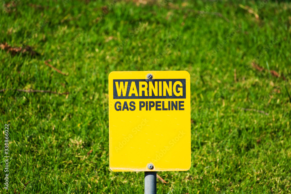 Warning gas pipeline sign with blurred background of green landscape