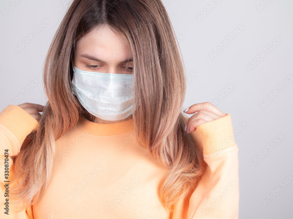 upset girl with a medical mask on her face straightens her hair