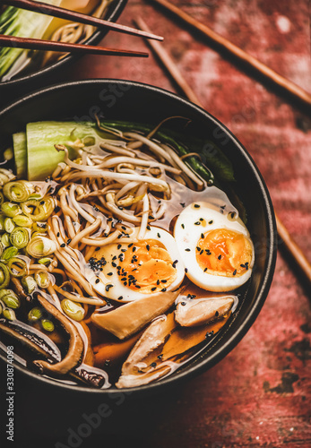 Traditional japanese Ramen soup with chicken meat and shiitake mushrooms in black bowls and bamboo chopsticks over dark red wooden table background, top view. Japanese cuisine concept