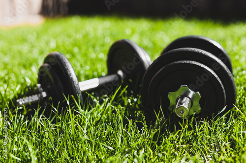 Fototapeta Naklejka Na Ścianę i Meble -  keeping fit and exercising outdoor, set of heavy dumbbells on green grass lawn in a backyard under direct sunlight
