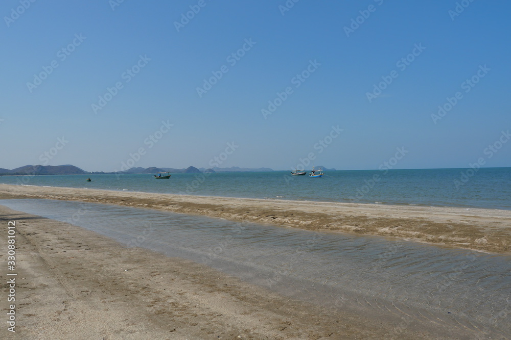 Sea wave splash the brown sand beach, Fishing boat float in the sea with island with mountain and blue sky in background, Khao Sam Roi Yot National Park , Prachuap Khiri Khan , Thailand
