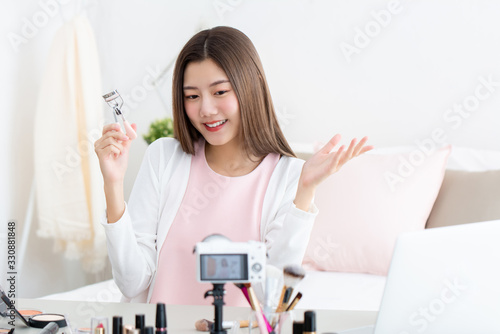 Young attractive asian woman beauty vlogger holding eyelash curler doing live streaming in front of camera