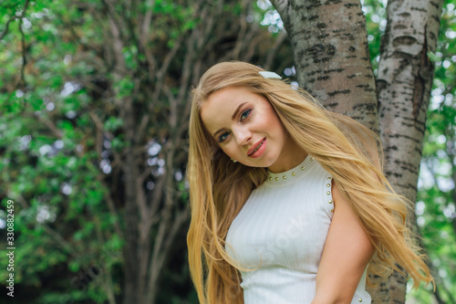 Portrait of a charming blond woman wearing beautiful white dress standing next to rowan tree.