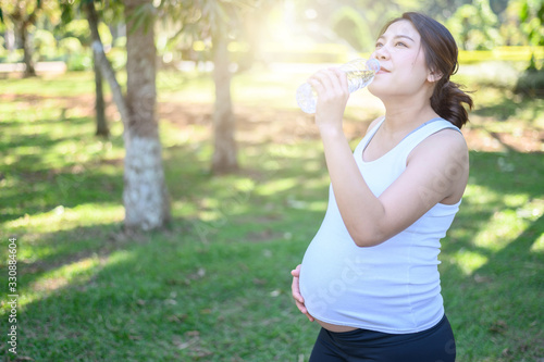 Portrait of young Asian pregnant woman drinking clean water after her relaxing and workout in the park. Conceptual of healthy and fitness pregnant woman can do exercise.
