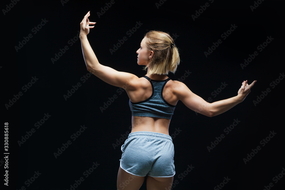 Back view of strong sporty girl in top and jean shorts showing muscles on black background Back view of strong sporty girl in top and jean shorts showing muscles on black background