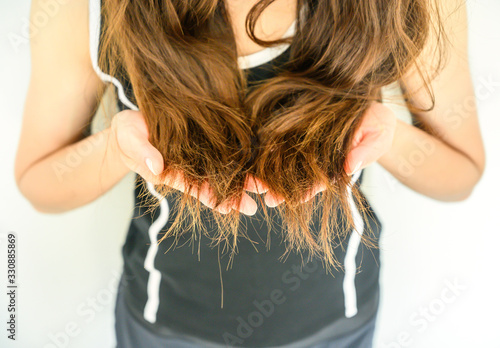 Cropped shot view of woman holding her damaged split ended hair (Focus at ends hair). Hair damage is risk for further damage and breakage. It may also look dull or frizzy and be difficult to manage.