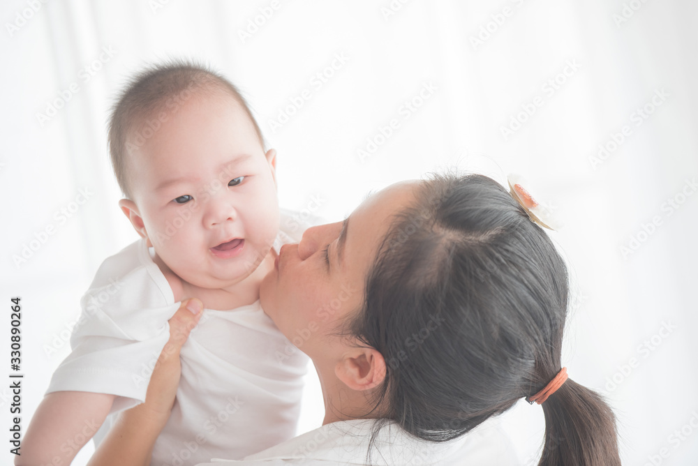 happy loving family. mother playing with her baby in the bedroom. asian mother hugging and holding her baby. family, motherhood, parenting, family and child care concept. White background. happy loving family. mother playing with her baby in the bedroom. asian mother hugging and holding her baby. family, motherhood, parenting, family and child care concept. White background.
