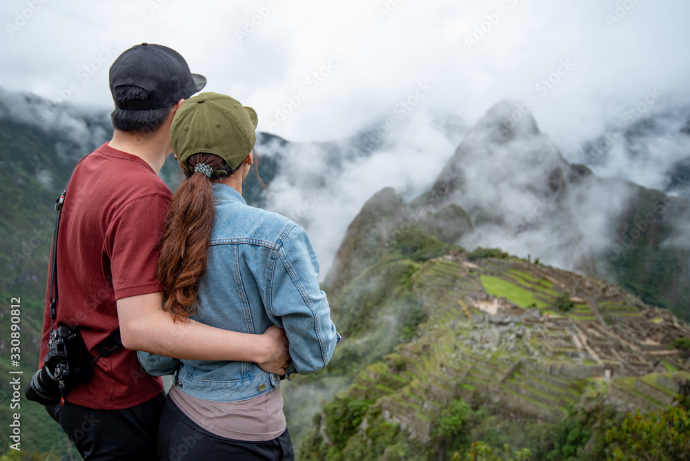 Asian couple tourist looking at Machu Picchu, one of seven wonders and famous tourist attraction in Cusco Region of Peru. This majestic place has known as 'Lost City of the Incas'