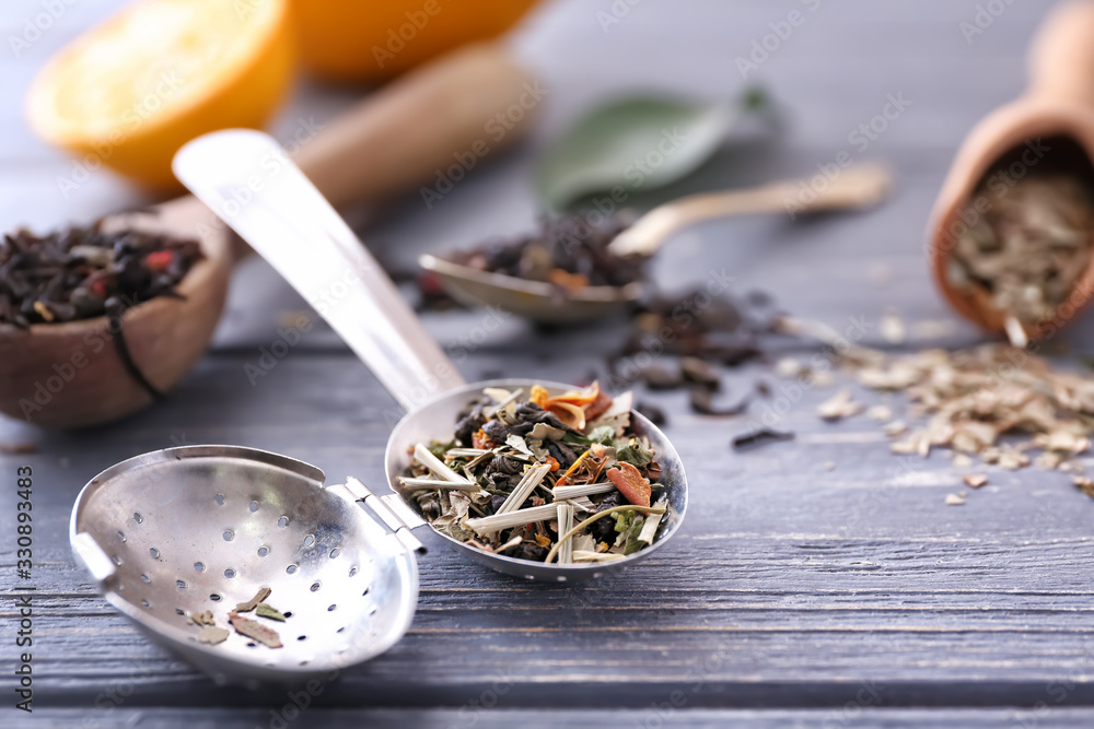 Strainer with dry tea leaves on wooden table