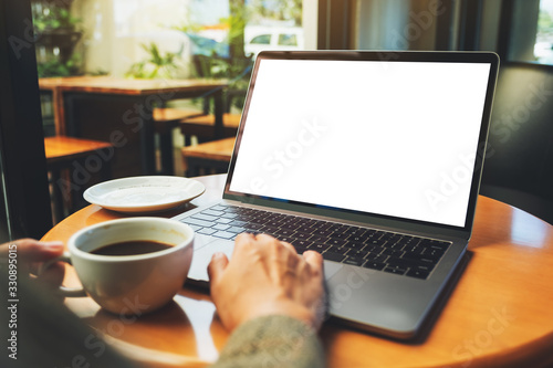 Mockup image of a woman using and touching on laptop touchpad with blank white desktop screen while drinking coffee cup