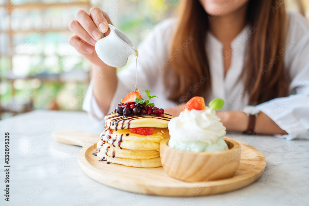 A beautiful woman pouring honey into a piece of mixed berries pancakes with ice cream and whipped cream A beautiful woman pouring honey into a piece of mixed berries pancakes with ice cream and whipped cream