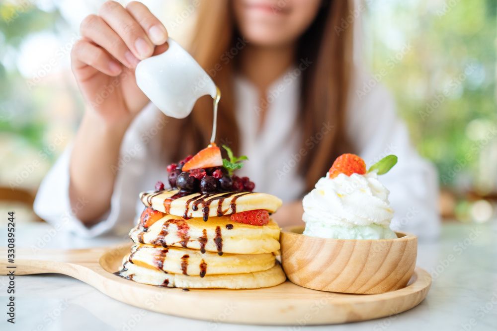 A beautiful woman pouring honey into a piece of mixed berries pancakes with ice cream and whipped cream A beautiful woman pouring honey into a piece of mixed berries pancakes with ice cream and whipped cream