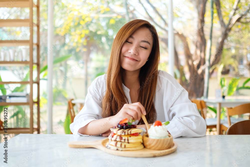 A beautiful asian woman eating ice cream and a mixed berries pancakes with whipped cream by wooden spoon A beautiful asian woman eating ice cream and a mixed berries pancakes with whipped cream by wooden spoon