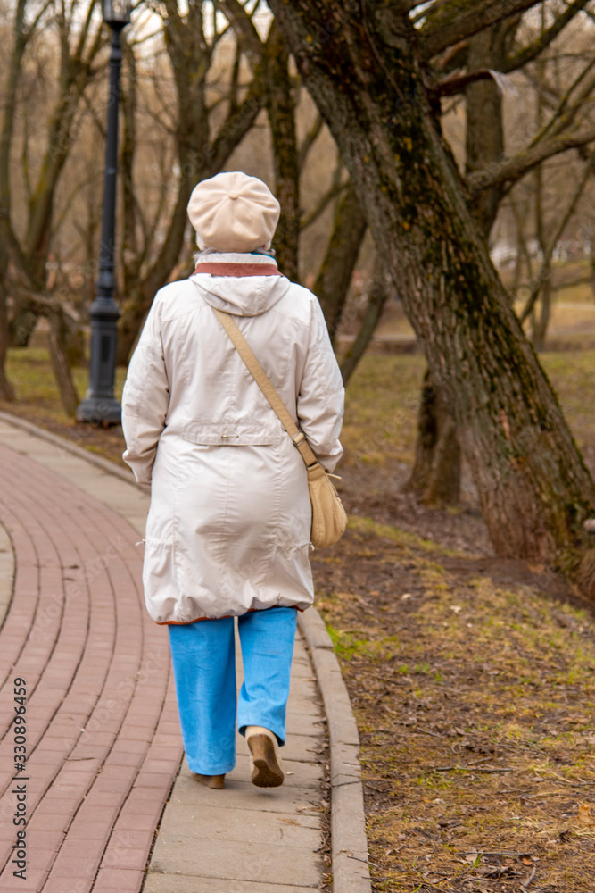 An elderly , elegantly dressed woman walks along an alley in a public Park