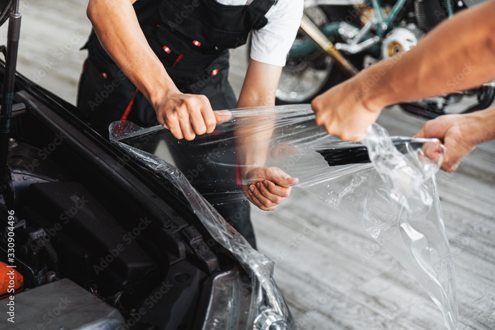 PPF installation process, close-up stretching removing an old transparent film on a car headlight and hood by hand. Automobile professional service.