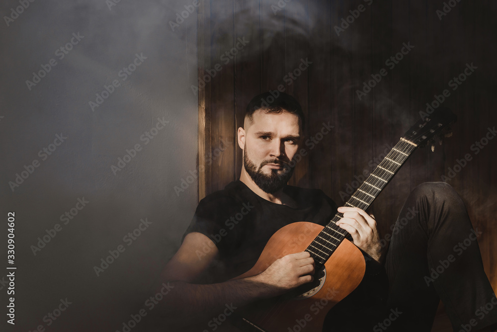 a man plays a guitar on a black background in the sun. romantic photo of a musician
