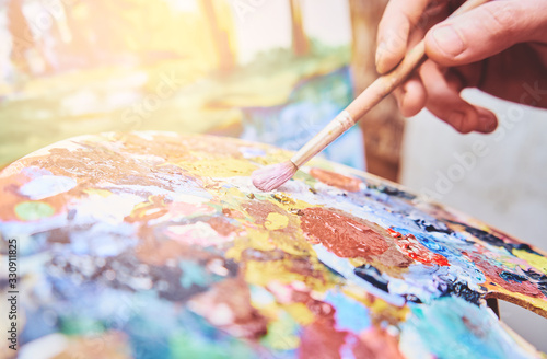 Close-up of brush in male hands mixing paints on a palette, soft focus, art creation
