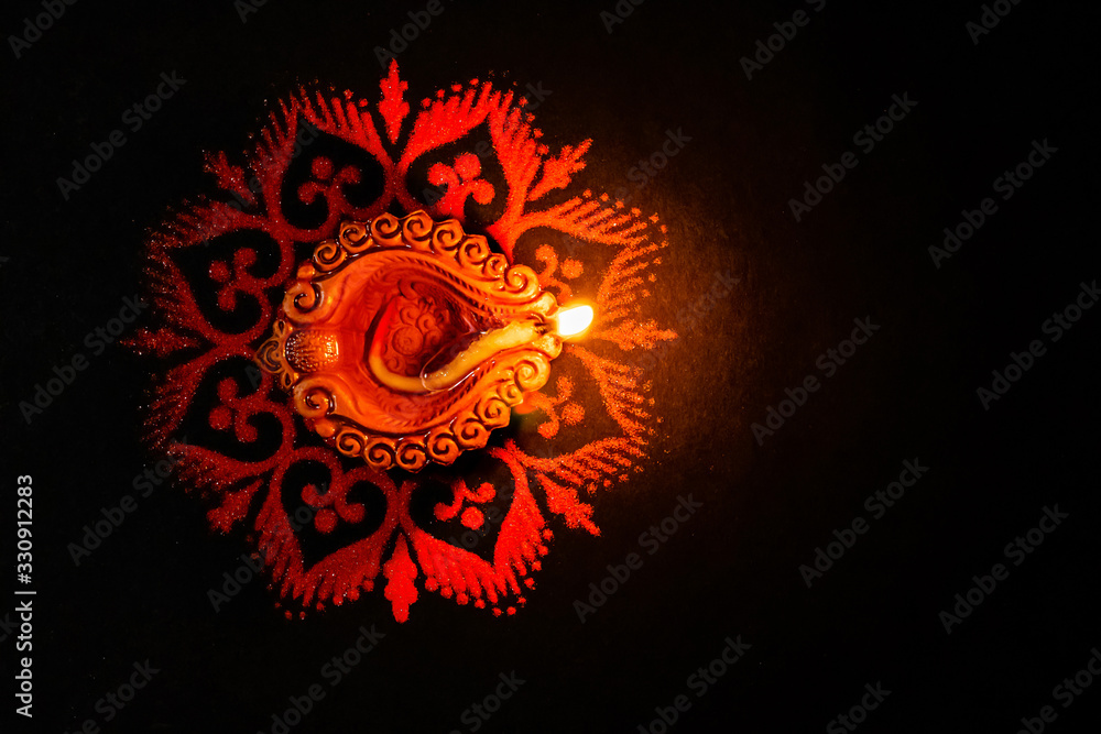 Fototapeta premium A Beautiful terracotta lamp glowing in the dark on a red rangoli with copy space on black background. dhanteras concept