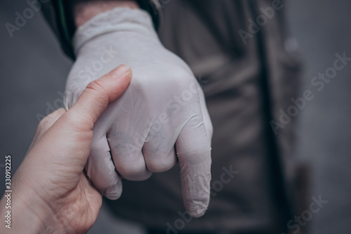 Two hands of a couple, one in a plastic glove, reaching each other. Virus protection concept, health issues. Closeup