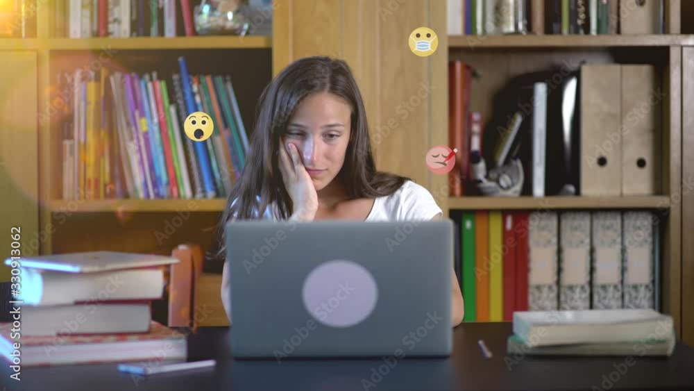 Worried young woman with red eyeglasses using social media on laptop reading bad news. Chat emojis emoticons that mean desease sick ill sufferers. Emoticons with face mask from the screen. Worried young woman with red eyeglasses using social media on laptop reading bad news. Chat emojis emoticons that mean desease sick ill sufferers. Emoticons with face mask from the screen.