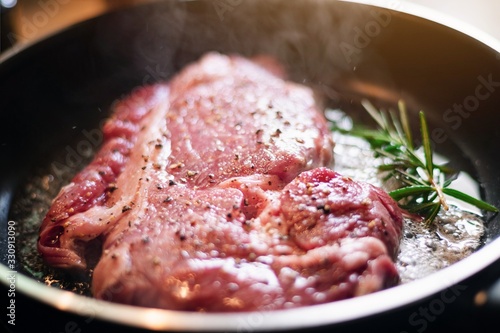 Raw fresh red beef steak and ingredients in frying pan with smoke