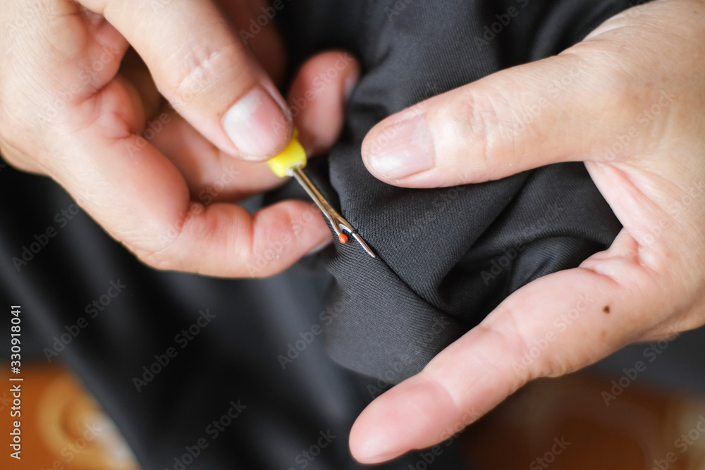 Hand of seamstress is tearing the thread out of the seam trousers close-up. Hand of seamstress is tearing the thread out of the seam trousers close-up.