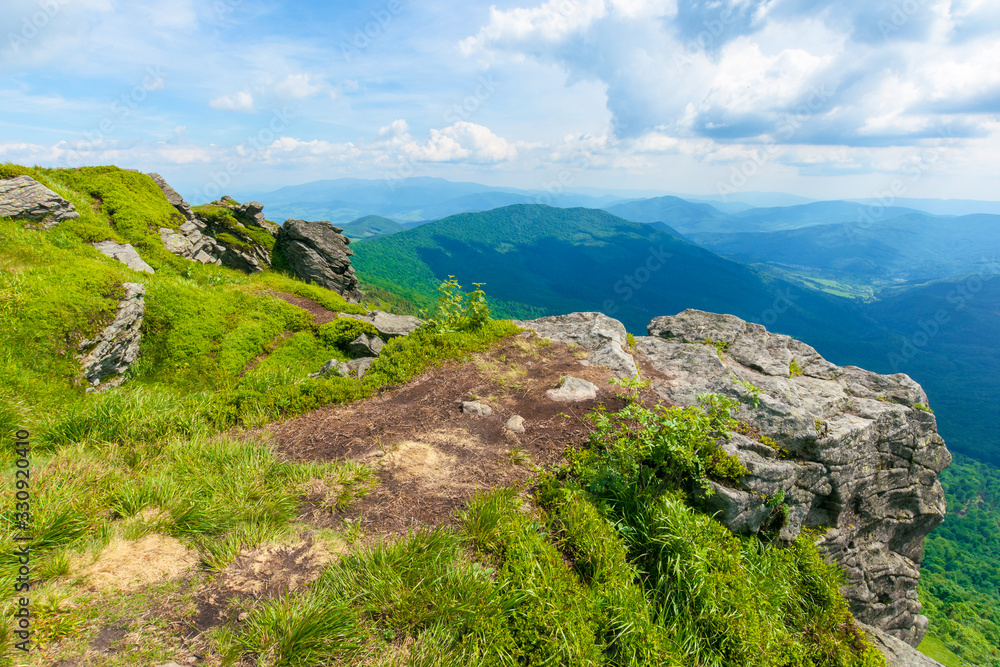 view in to the valley from the top of a mountain. huge rocks on the grassy hillside. clouds on the sky. beautiful sunny weather with dappled light. freedom in tourism concept view in to the valley from the top of a mountain. huge rocks on the grassy hillside. clouds on the sky. beautiful sunny weather with dappled light. freedom in tourism concept