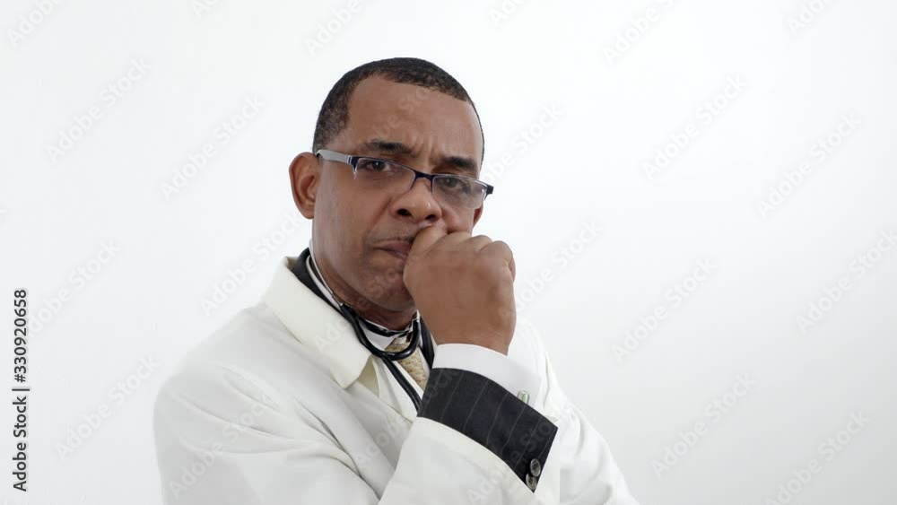 Jamaican African-American man doctor in white lab coat in glasses, turning head looking at the camera with serious concern over white wall background isolated. Jamaican African-American man doctor in white lab coat in glasses, turning head looking at the camera with serious concern over white wall background isolated.