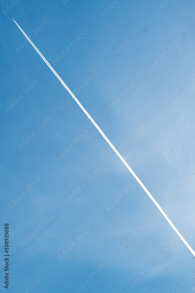 White trail from an airplane on a bright blue sky among the clouds. A plane flies high in the sky. White trail from an airplane on a bright blue sky among the clouds. A plane flies high in the sky.