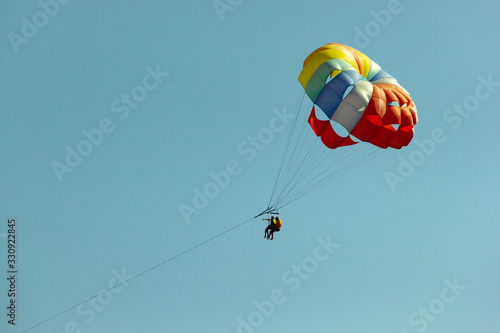 Multicolored parachute against the blue sky. Happy couple Parasailing in summer.