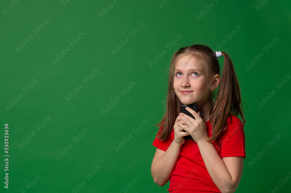 happy little model girl smiling holding smartphone dreamily looking up on green background