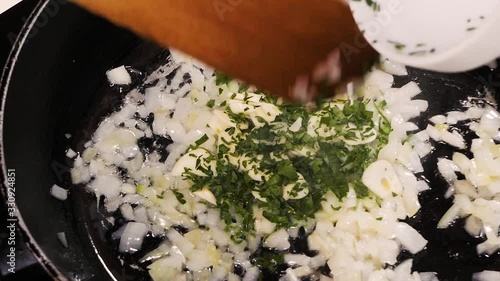 In a finely chopped fried onion in a pan, the cook adds garlic and herbs.